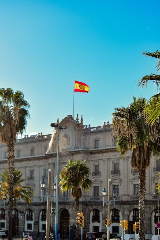 A majestic historic building with a Spanish flag waving against a clear blue sky in Barcelona.